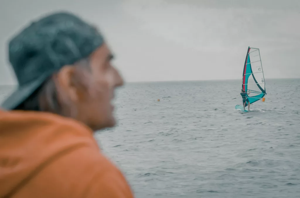 Portrait flou d'Antoine Albeau en premier plan, avec un véliplanchiste en action sur la mer en arrière-plan, pour le projet Néo Portrait par gcom.