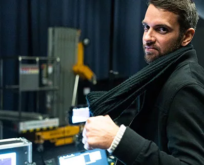 Portrait d'un collaborateur de l'agence gcom prenant la pose avec son écharpe devant le matériel de régie technique et les flight-cases.