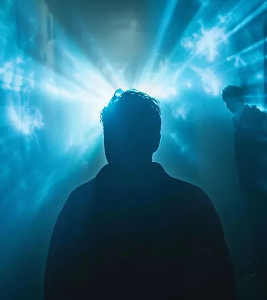 Silhouette d'homme de dos face à des projecteurs puissants dans la brume, illustrant la vision de l'agence gcom pour 2026 : transformer l'incertitude en communication fondée sur des récits utiles.