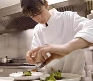 Zian Bodou, jeune chef de 19 ans, en pleine préparation d'un plat gastronomique dans la cuisine professionnelle de son restaurant.