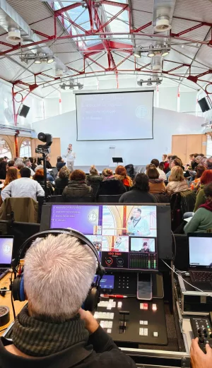 Vue de dos d'un technicien gcom aux commandes d'une régie vidéo lors d'une conférence à l'INSET de Bordeaux. Sur les écrans de contrôle : orateurs et diapositives.